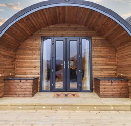 A wooden glamping pod with a wooden deck two storage benches and black framed glass double doors at The Stag - Crossgate Luxury Glamping in Hartsop near Glenridding