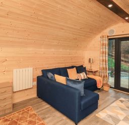 A living area with a blue sofa with pillows near glass doors and wooden walls at The Stag - Crossgate Luxury Glamping Hartsop near Glenridding