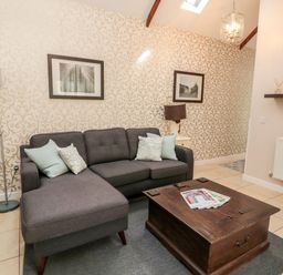 A living room with a gray sectional sofa and pillows a wooden coffee table and patterned wallpaper at Kizzie Cottage in Guyzance near Warkworth