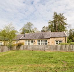 A stone cottage with white windows and a wooden fence in front with a grassy yard at Kizzie Cottage Guyzance near Warkworth