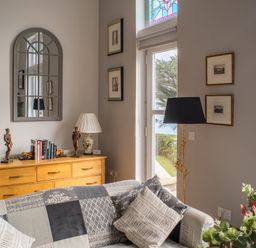 A living room with a patterned sofa cushions floor lamp wooden sideboard with books and sculptures and framed pictures on the walls at King Edward's View in Newquay