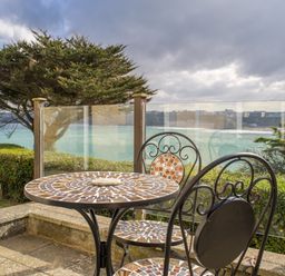 A patio with a mosaic table and two chairs overlooking the ocean with glass railing at King Edward's View in Newquay