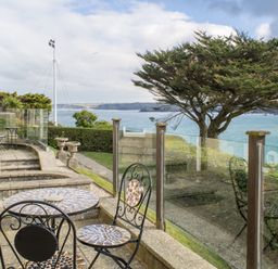 A patio with mosaic table and chairs overlooking a tree hedge and sea at King Edward's View in Newquay