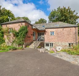 A brick house with a sloped roof and stairs leading to the front door surrounded by trees and plants at The Old Watermill in St Mabyn