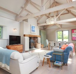 A living room with sofas a fireplace a dining table and large wooden beams at The Old Watermill in St Mabyn