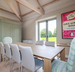 A dining room with a wooden table white chairs striped upholstered chairs and a large framed artwork near French doors at The Old Watermill in St Mabyn