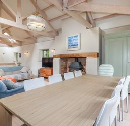 A dining table with white chairs next to a fireplace and sofas in a living room at The Old Watermill in St Mabyn