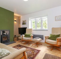 A living room with beige chairs a green feature wall and a television at Yamthwaite in Grizedale near Hawkshead