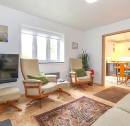 A living room with two armchairs with green cushions a wall mounted TV and a patterned rug at Yamthwaite in Grizedale near Hawkshead
