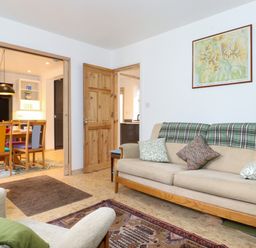 A living room with a beige sofa with cushions and a plaid blanket a framed map on the wall and doorways leading to a dining area and kitchen at Yamthwaite in Grizedale near Hawkshead