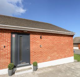 A front entrance of a brick house with a dark door and two potted plants on either side at The Hawthorns in Llanfechell