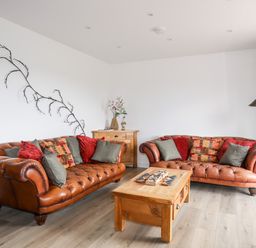 A living room with two brown leather sofas red and gray cushions wooden coffee table and cabinet with flower vase at The Hawthorns in Llanfechell