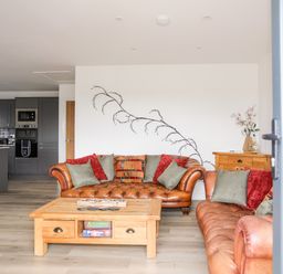 A living room with two brown leather sofas and a wooden coffee table next to a kitchen with grey cabinets at The Hawthorns in Llanfechell