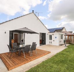 A patio area with outdoor dining furniture and an umbrella next to a white house with a garden at The Hawthorns in Llanfechell