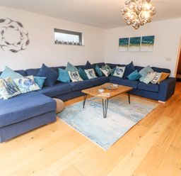 A living room with a large blue sectional sofa with multiple cushions a wooden coffee table and a wall decoration at Tregenna House in St Ives