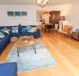 A living room with a blue sectional sofa and wooden coffee table next to a dining area at Tregenna House in St Ives