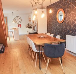 A dining area with a wooden table and chairs next to a kitchen with stools and a wall clock at Tregenna House in St Ives