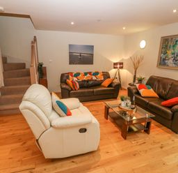 A living room with brown and white sofas a glass coffee table and a staircase at Barn End 9 Stad Clynnog in Newborough