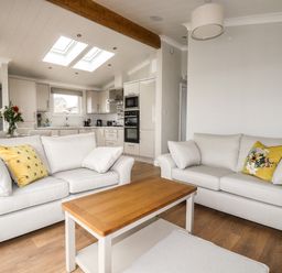 A living room with two sofas a wooden coffee table and a kitchen with skylights at Acorn Lodge in St Day