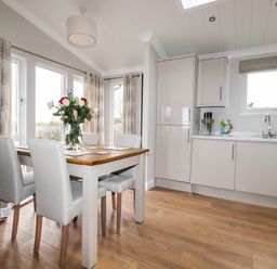 A kitchen and dining area with a wooden table set with flowers and chairs near windows at Acorn Lodge in St Day