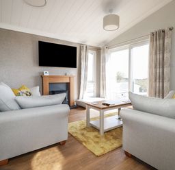 A living room with two sofas a wall mounted TV a fireplace and a coffee table at Acorn Lodge in St Day
