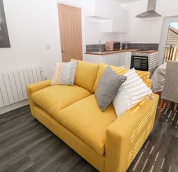 A yellow sofa with cushions in a living area adjacent to a kitchen and dining table with chairs at Perran Pearl A in Perranporth