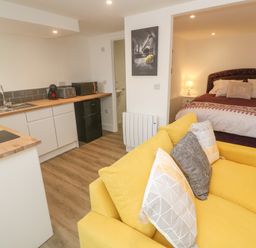 A studio apartment with yellow sofa and kitchen area next to a bed at Perran Pearl B in Perranporth