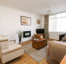 A living room with armchairs a sofa a wooden coffee table a television and a wall-mounted electric fireplace at Beach Side in West Bay