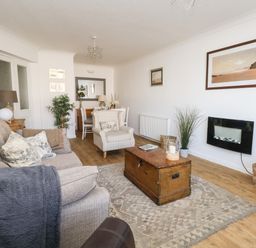 A living room with a sofa armchair wooden chest as coffee table wall-mounted fireplace and dining table at Beach Side in West Bay