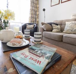 A living room with a wooden coffee table holding a teapot cups pastries books and a vase of flowers at Beach Side in West Bay