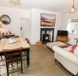 A living room with a wooden dining table and chairs a sofa and ottoman a stove fireplace a television and a blue sideboard at Rhytty Bach in Ty Croes near Rhosneigr