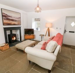 A living room with a beige sofa and ottoman a wood burning stove and a television at Rhytty Bach in Ty Croes near Rhosneigr