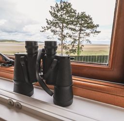 Binoculars on a wooden window sill with a view of a tree and landscape at Oversands Cottage in Grange-Over-Sands