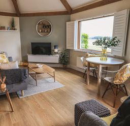 A living room with sofa, coffee table, TV, round dining table with chairs, and large window at Oversands Cottage in Grange-Over-Sands