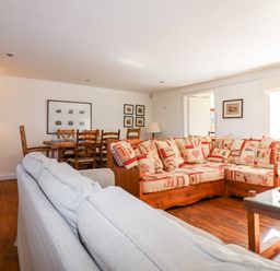 A living room with a patterned wooden sofa a grey fabric sofa a dining table with wooden chairs and framed pictures on walls at 1 The Lane in Chipping Norton