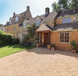 A traditional stone house with a gravel driveway and green lawn at 1 The Lane in Chipping Norton