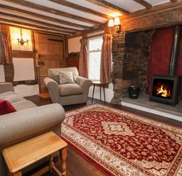 A living room with a sofa and armchair near a wood burning stove on a patterned rug at 18 Church Street in Llangollen