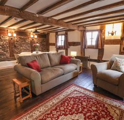 A living room with two grey sofas a red patterned rug wooden beams and a dining table with flowers at 18 Church Street in Llangollen