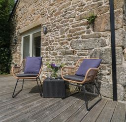 Two wicker chairs with cushions and a small table with drinks on a wooden deck outside a stone building at The Reading Room in Seworgan near Constantine