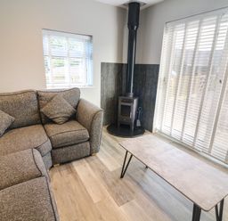 A living room with a gray corner sofa a wood burning stove and a table at White Stones in Goadsbarrow near Roose