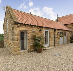 A stone building with a tiled roof and gravel ground with potted plants outside at Foxglove in Goathland
