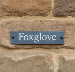 A rectangular sign with the word Foxglove on a stone wall at Foxglove in Goathland