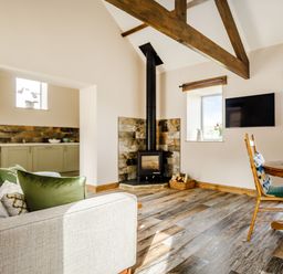 A living room with a sofa, wood stove, dining table, and kitchen area at Foxglove Goathland