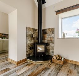 A corner fireplace with a wood stove and basket of firewood next to a window with flowers at Foxglove in Goathland