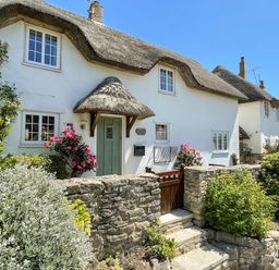 A thatched roof cottage with a green door surrounded by stone walls and flowering bushes at Cajun Cottage in West Lulworth