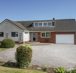 A detached house with a gravel driveway and garden shrubs at Eildon Lodge in Gosforth