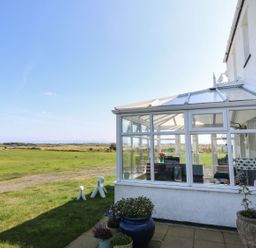 A glass conservatory attached to a white house with potted plants outside and a grassy field in the background at Trewan House Bryngwran near Rhosneigr Rhosneigr