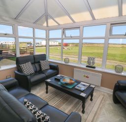 A seating area with black leather sofas and a coffee table in a glass conservatory overlooking a grassy field at Trewan House Bryngwran near Rhosneigr Rhosneigr