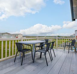 A deck with a table and four chairs overlooking grassy land and mobile homes at Trewan Lodge in Bryngwran near Rhosneigr