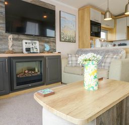 A living room with a fireplace television sofa and coffee table with flowers at Trewan Lodge Bryngwran near Rhosneigr